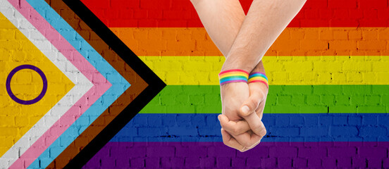 lgbtq, trans and intersex rights concept - close up of male couple hands with rainbow wristbands...