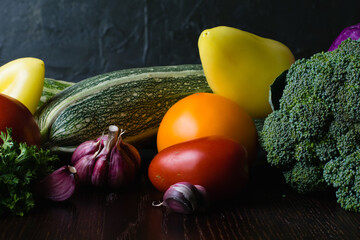 Vegetables tomatoes, peppers, garlic, zucchini, cabbage on a dark wooden table, side view. Concept of vegetarianism and proper nutrition.