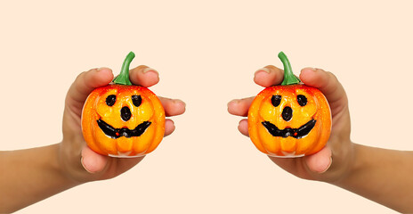 Festive background for Halloween. A young girl's hand holds a small orange pumpkin for Halloween on the background of the color trend #FAEBD7 Champagne 2021. Smiling Jack Lantern. Fear