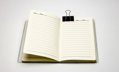 Open notebook on white background with an attached black binder clip