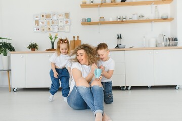 Happy mother hugging daughter and son sitting on wooden floor in modern kitchen at home. Mom hugging children. Happy family relationship concept