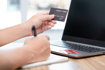 Hand a man hold credit and use pen white on the book and laptop computer on wood table : home shopping and delivery concept