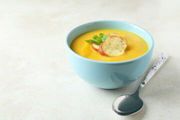 Plate of pumpkin soup and spoon on white textured table
