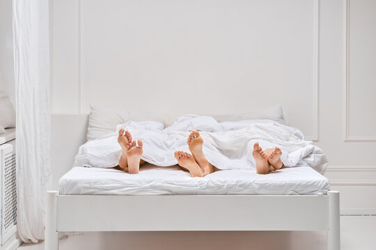 Three pairs of female legs sticking out from under the blanket