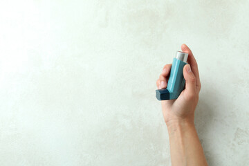 Female hand holds blue asthma inhaler on white textured table - obrazy, fototapety, plakaty
