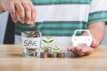 Save money concept. Man's hand dropping a coin in a piggy bank coins collected in a glass and stacked coins were placed on a wooden table and car symbol.
