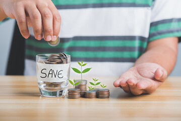 Save money concept. Man's hand dropping a coin in a piggy bank coins collected in a glass and stacked coins were placed on a wooden table .