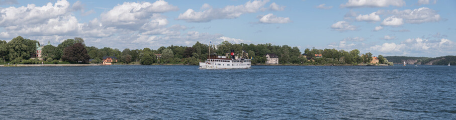 Obraz premium Old steam boat arriving Stockholm from the archipelago passing the island Djurgården