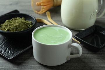 Cup of matcha latte and accessories for making on gray textured table