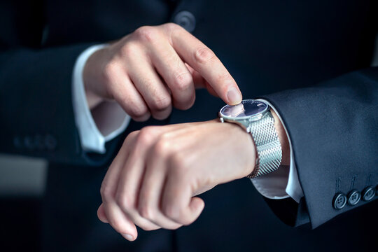 Watch around the wrist of a stylish business man. Busy businessman looking at the time. Stress or hurry at work. Person wearing suit and pointing at his wristwatch with finger. Deadline or overwork. - Powered by Adobe