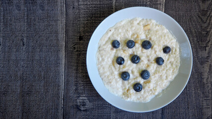 on the right, oatmeal porridge with banana, coconut milk and blueberries lies in a light gray plate on a wooden table. top view