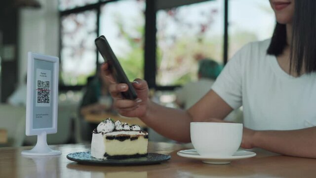 Customer Asia women using phones for scanning QR code for pay dessert. Mobile scanning system online for pay money on cafe. Concept technology for social distance.