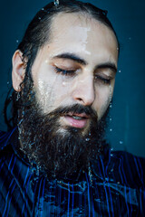 Very close-up portrait of a young bearded man with closed eyes and streams of water running down...