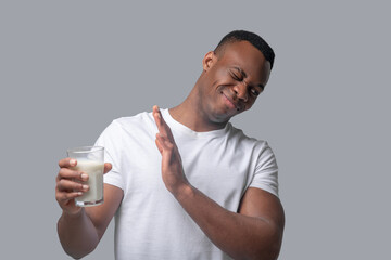A dark-skinned man in a white thsirt holding a glass with milk