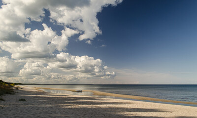 Obraz premium Sea shore on a sunny day with large, white cumulus clouds.
