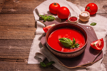 Tomato soup with basil in a bowl. Ripe vegetables, fresh greens, fragrant spices. Vintage wooden table, copy space