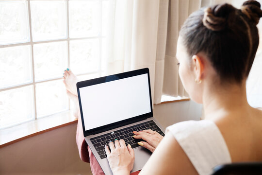 A Young Woman Types On Her Laptop. She Is Relaxed In Front Of The Window With A Boyish Hairstyle.