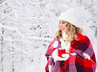 Beautiful happy smiling young woman in warm clothing with red cup of hot drink on cold snowy winter outdoors. Girl hands in gloves holding mug with hot cocoa, tea, coffee. Winter, Christmas time