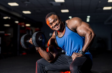 Fototapeta na wymiar Strong african man in a gym. Handsome man with big muscles smiling toothy while posing to the camera in a gym