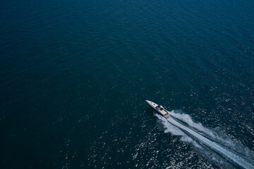 Large boat on the water in motion top view. Luxury motor boat on dark blue water aerial view. Speedboat is fast moving in dark water. Travel on high-speed boats on the water.