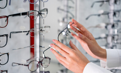 Row of glasses at an opticians. Eyeglasses shop. Stand with glasses in the store of optics. Woman's hand chooses spectacles. Eyesight correction