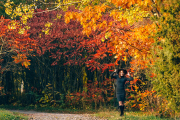 Beautiful woman in a dark dress stands in a park on the background of yellowed trees. Autumn background