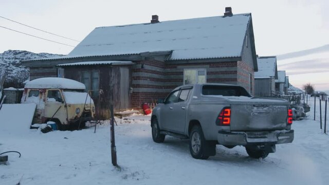 Modern car with a running engine and an old rusty truck in the snow near a brick house