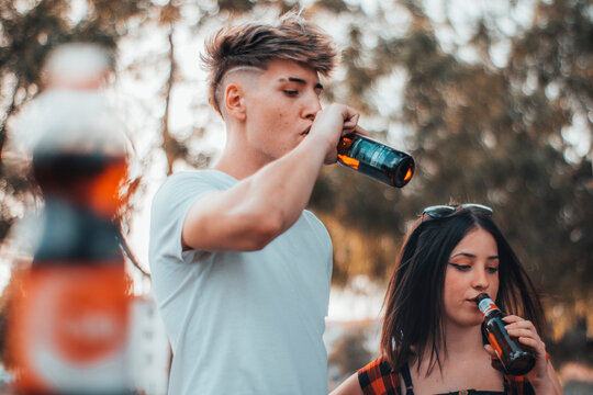 Hombre joven y chica bebiendo cerveza en una barbacoa al aire libre junto a los colegas