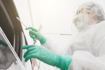 Doctor in protective suit PPE holding test kit. Medical worker performing drive-thru Covid-19 test, taking nasal swab sample patient through car window, PCR diagnostic, Rapid antigen test kit (ATK)