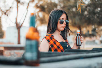 Mujer joven con gafas de sol y cervezas cocinando una barbacoa de amigos al aire libre
