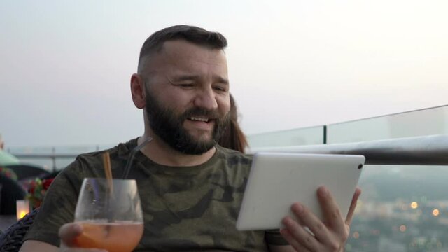 Young Man Watching Movie On Tablet Sitting At Luxury Rooftop Restaurant