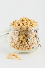 Peeled pine nuts in a glass jar on a light background.