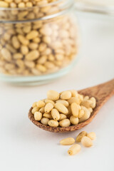 Peeled pine nuts on a wooden spoon and in a glass jar on a light background.