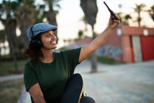 Portrait of happy african-american woman taking selfie photo outdoors. Happy woman sitting and listening the music