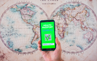 Fototapeta na wymiar Human male hand holding mobile phone with green card passport, health certificate of vaccination of Covid-19 for travel