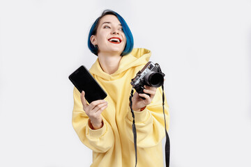 A female photographer in yellow hoody holding a camera and smarphone.