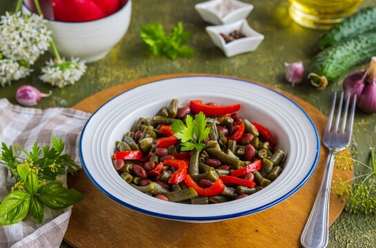 Warm salad or vegetable stew made from asparagus beans, canned red beans and roasted red bell peppers in a white plate on a green concrete background. Beans recipes. Vegan food.