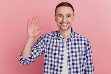 Friendly smiling man waving hand to greet you make hi gesture and looking happy to see you standing over pink background