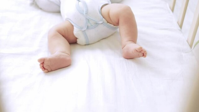 the feet of a small child lying in a crib on a white cotton bed at home close-up, the heels of a newborn sleeping baby