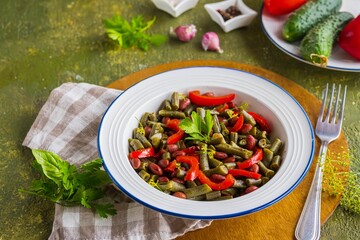 Warm salad or vegetable stew made from asparagus beans, canned red beans and roasted red bell peppers in a white plate on a green concrete background. Beans recipes. Vegan food.
