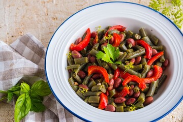 Warm salad or vegetable stew made from asparagus beans, canned red beans and roasted red bell peppers in a white plate on a light concrete background. Beans recipes. Vegan food.