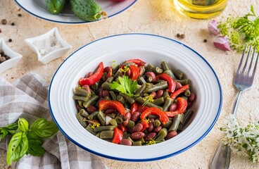 Warm salad or vegetable stew made from asparagus beans, canned red beans and roasted red bell peppers in a white plate on a light concrete background. Beans recipes. Vegan food.