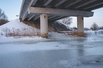 reflection from the pillars under the bridge in winter on the ice of the river. big transport...