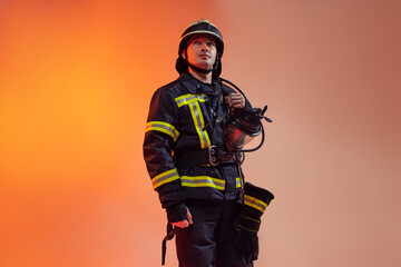 One male firefighter dressed in uniform posing over orange background in neon lights.