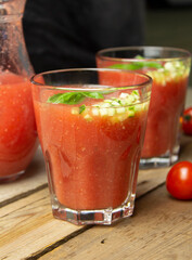 Gazpacho tomato soup in glasses with cucumber and basil leaves on a wooden table