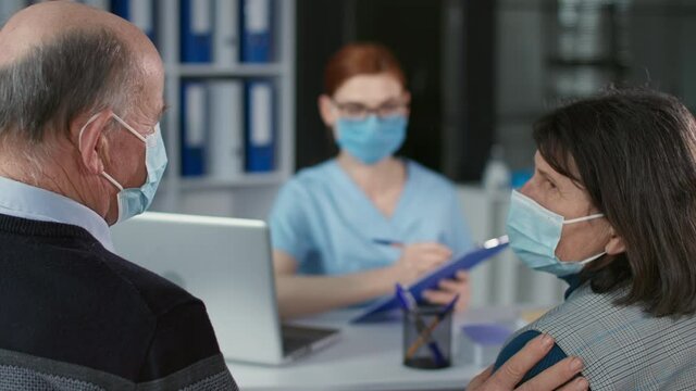 portrait of female doctor wearing mask and gloves to protect against virus and infection, consults an elderly couple on state of their health