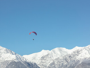 Fototapeta na wymiar the red wing of the paraglider against the background of the blue sky and the snow-white peaks of the high mountains. the parachutist during the flight against the background of the Alpine mountains