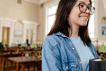 Young white woman in eyeglasses smiling while standing with book