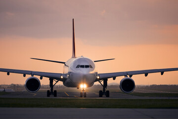 Wide-body airplane taxiing for take off. Front view of plane against airport at sunset..