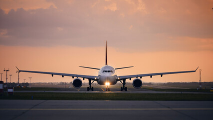 Wide-body airplane taxiing for take off. Front view of plane against airport at sunset..